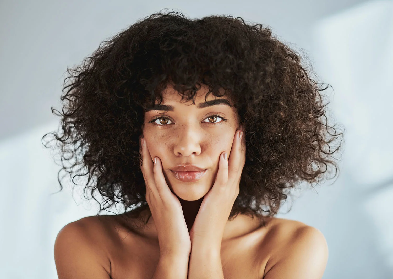 Woman with curly hair holding her hands to her face.